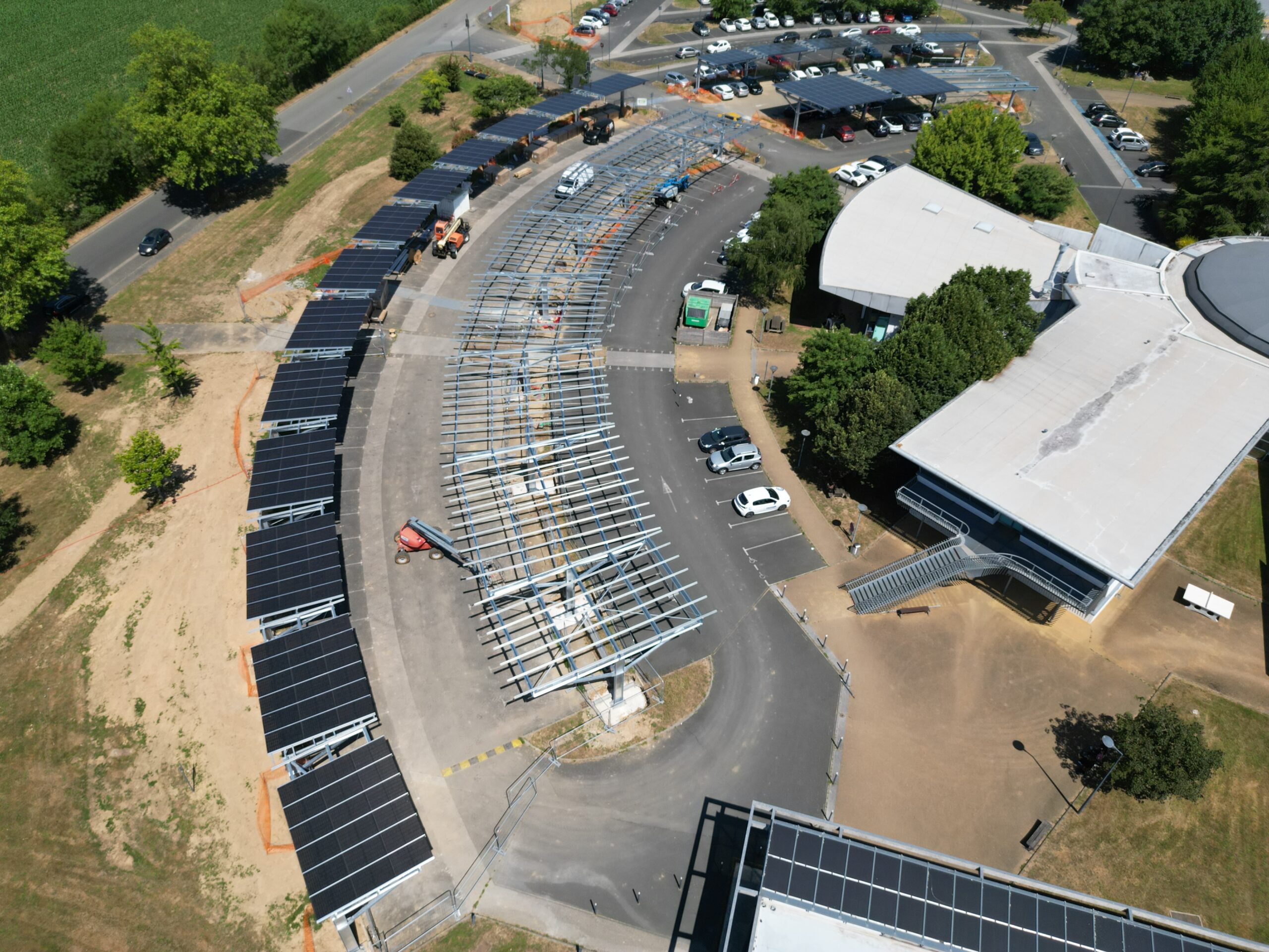 Vue aérienne d'un parking avec des panneaux solaires installés et un bâtiment moderne.
