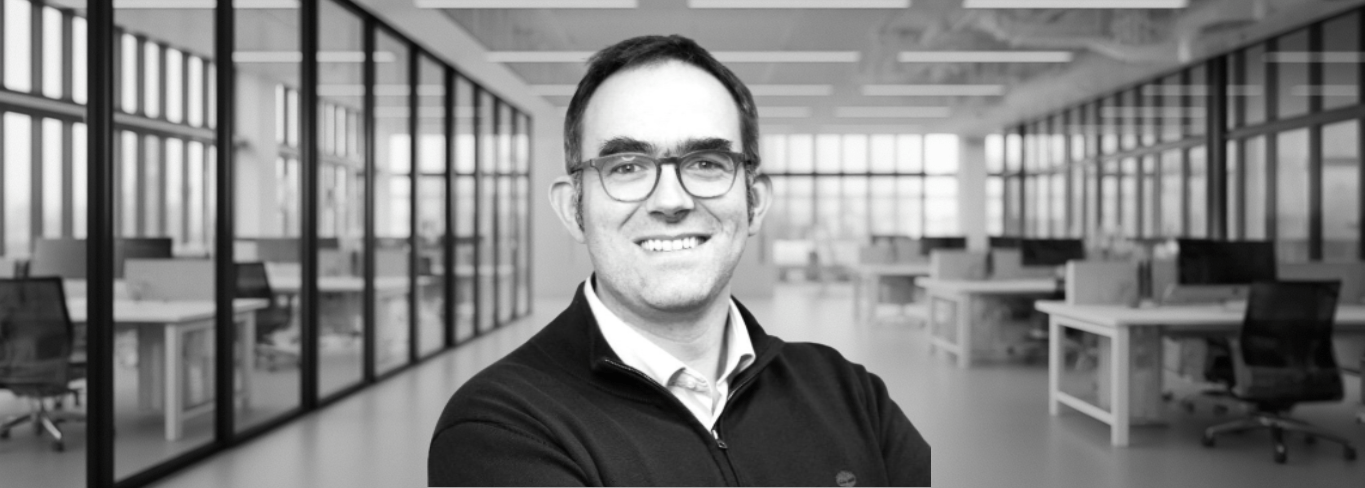 Portrait d'un homme souriant dans un bureau moderne.