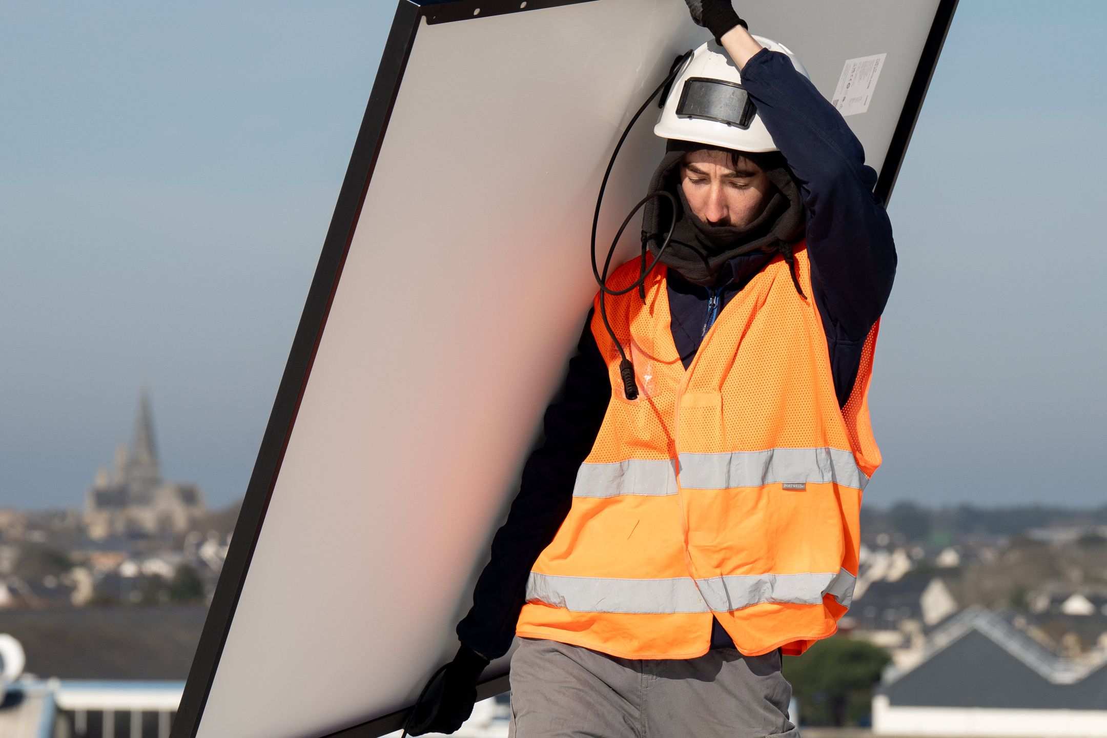 Person en gilet de sécurité portant un panneau solaire sur le toit