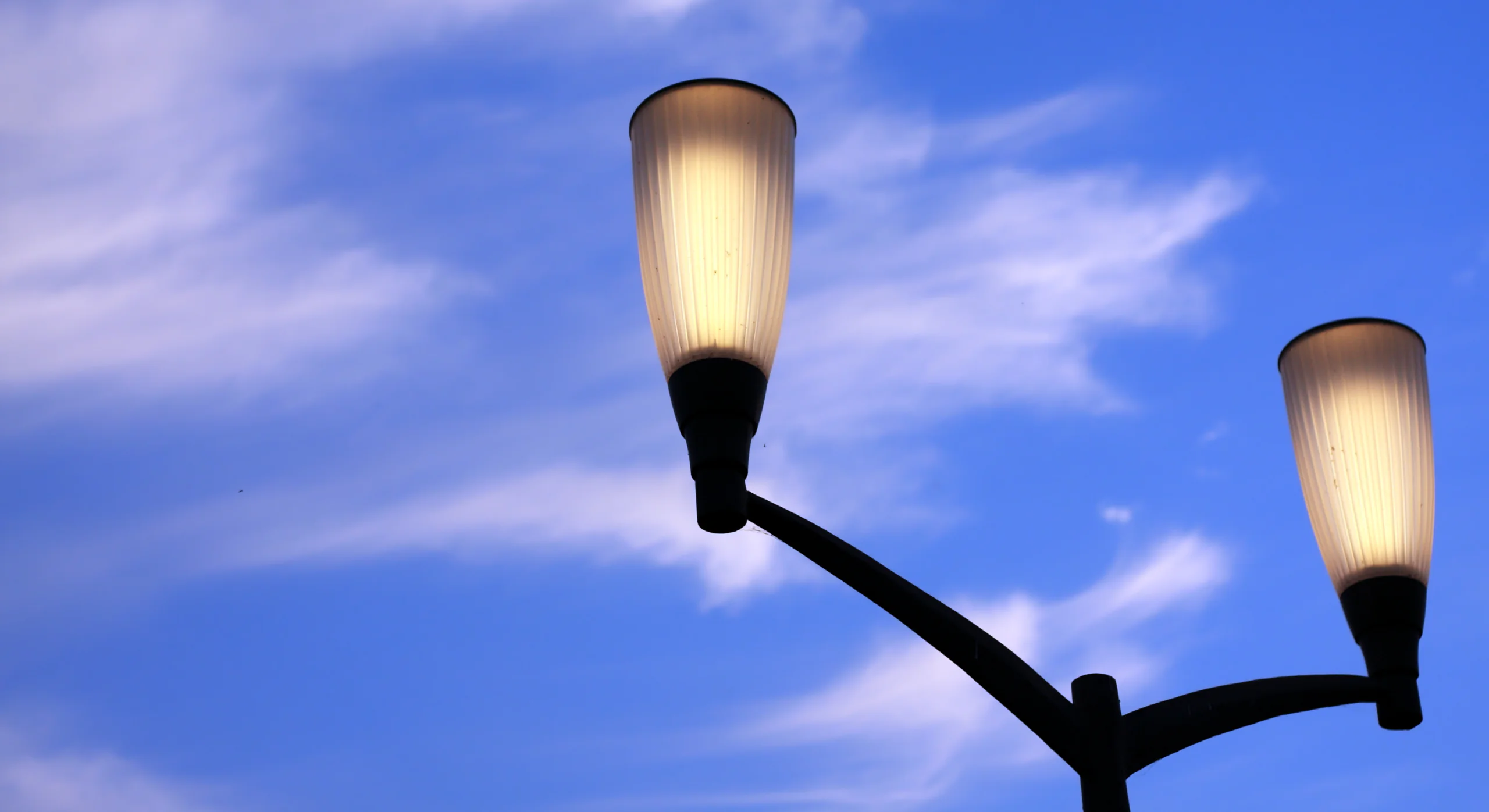 Lampadaires allumés sous un ciel bleu et nuageux, symbolisant l'éclairage public et l'énergie.